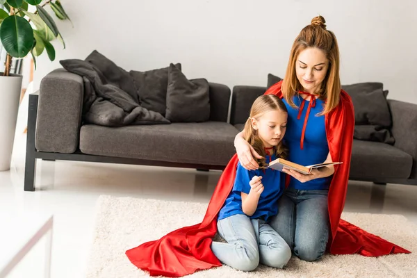 かわいい子供と床で本を読んで座っている赤いマントの母 — ストック写真