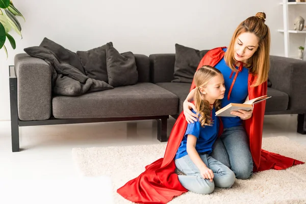 子供と母床と本を読んで座っている赤いマントで — ストック写真