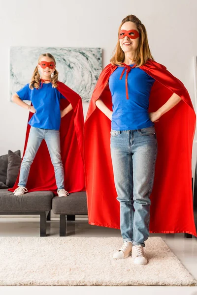 Schattige Dochter Moeder Rode Mantels Maskers Staan Met Handen Heupen — Stockfoto