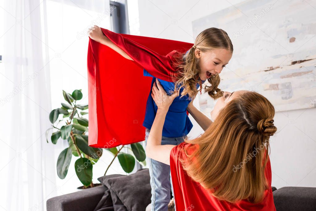 smiling mother and kid in red cloaks playing at home