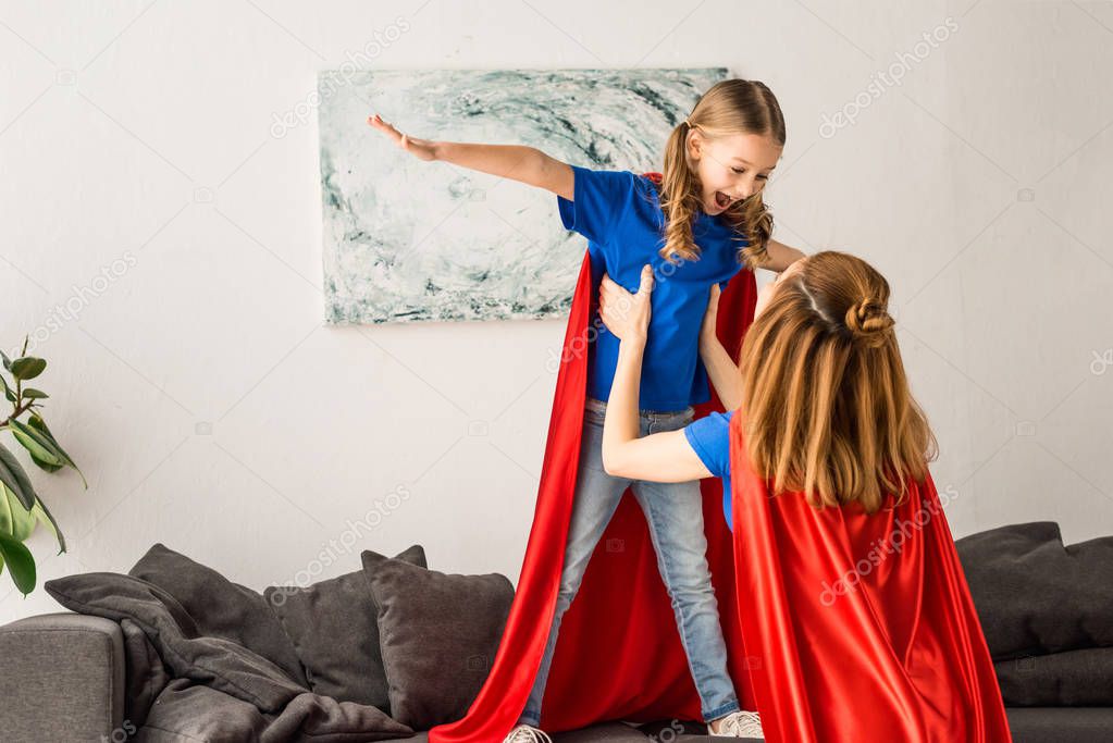 Mother and kid in red cloaks having fun at home