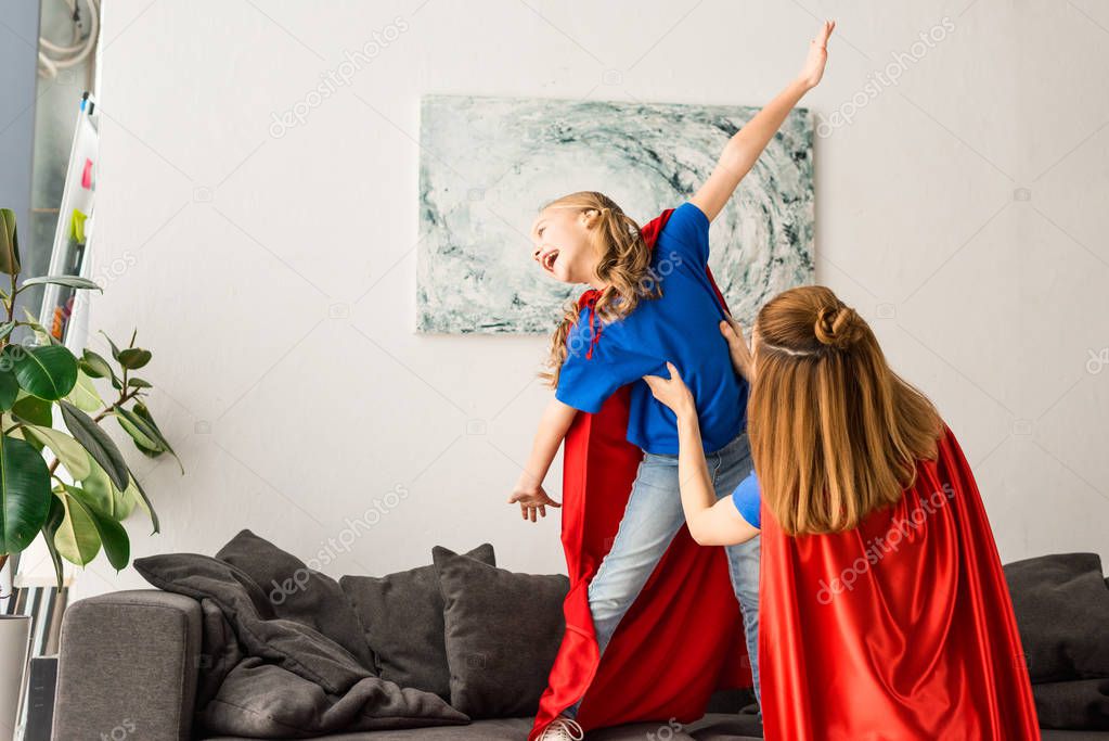 Kid and mother in red cloaks playing and smiling at home 
