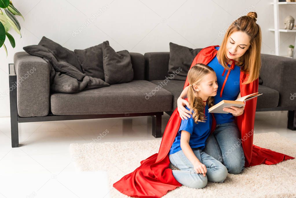 kid and mother in red cloaks sitting on floor and reading book