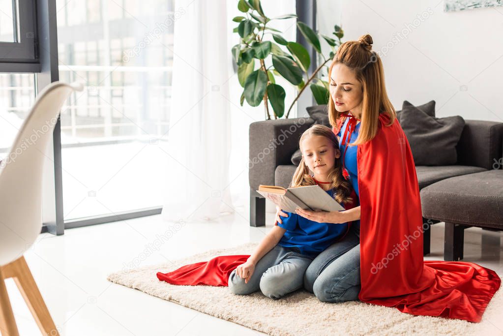 daughter and mother in red cloaks sitting on floor and reading book