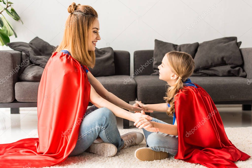 daughter and mother in red cloaks sitting on floor and looking at each other