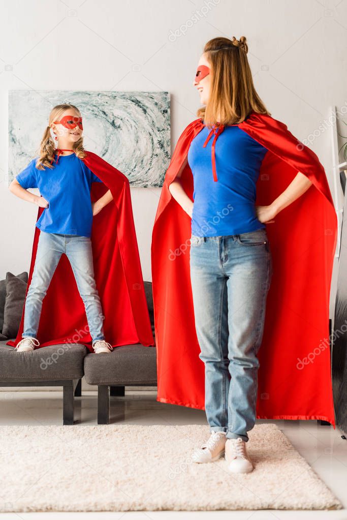 Cute daughter and mother in red cloaks and masks looking at each other