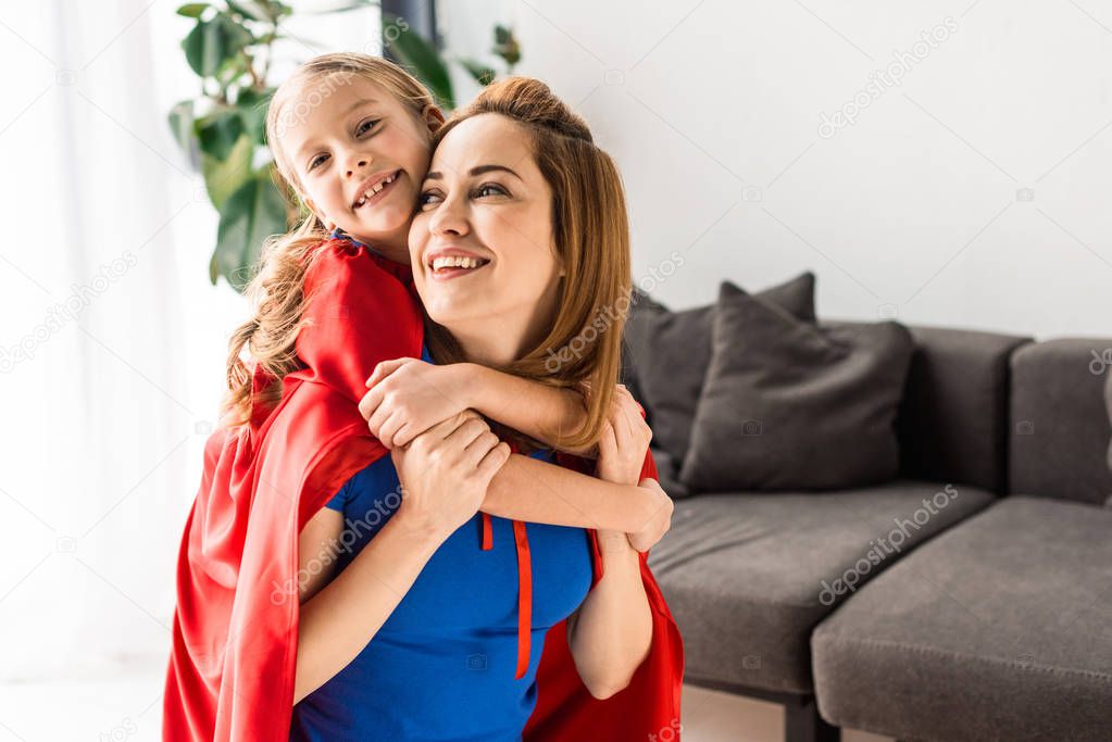 daughter and mother in red cloaks hugging and smiling at home 