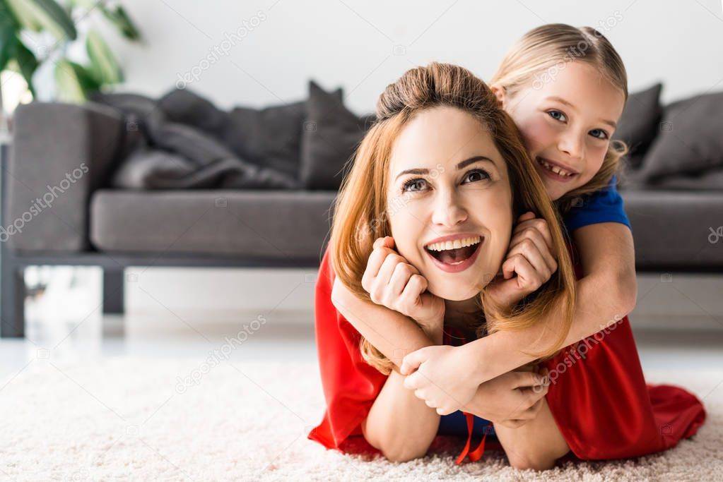 Cute kid and attractive mother hugging on floor