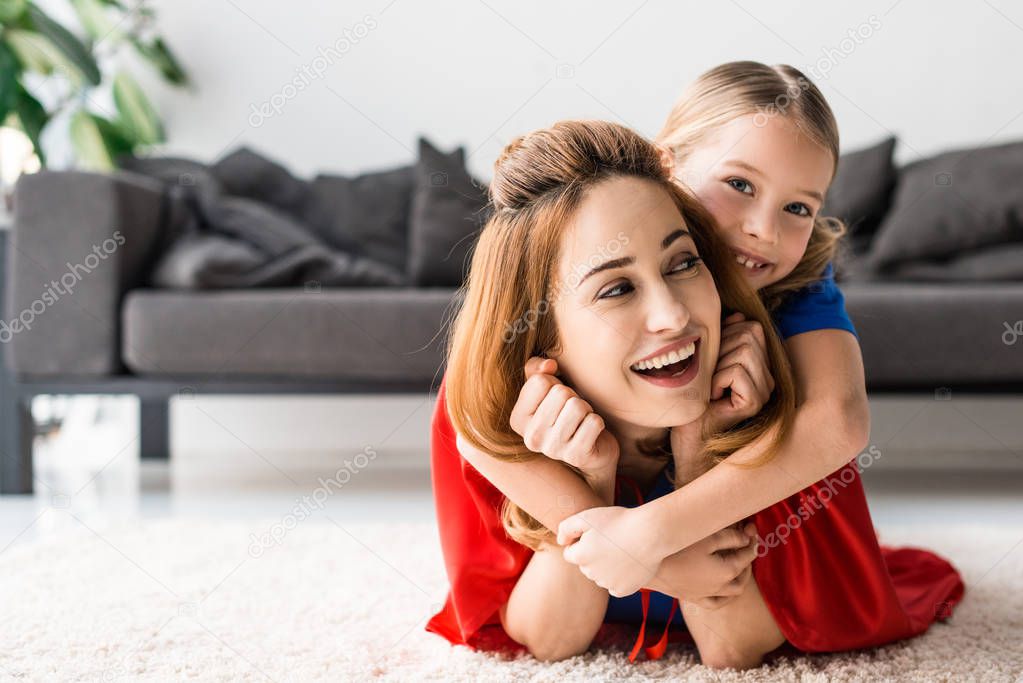 Cute daughter and attractive mother hugging on floor