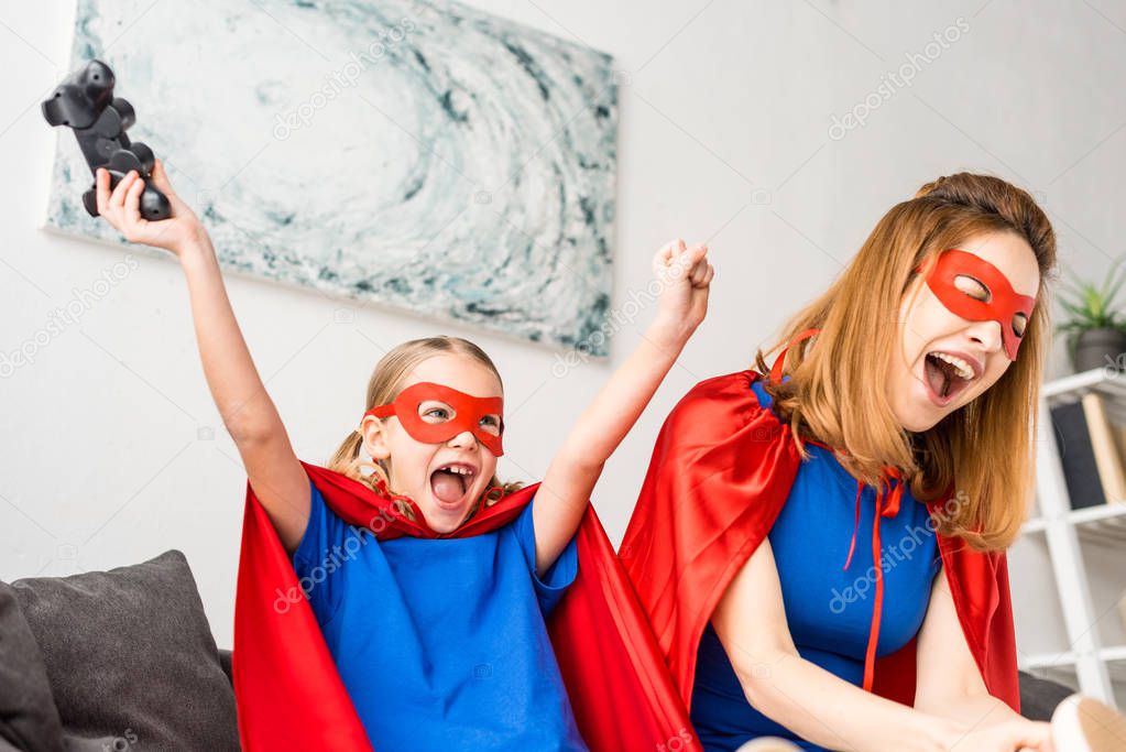 Mother and daughter in red masks and cloaks playing video game at home