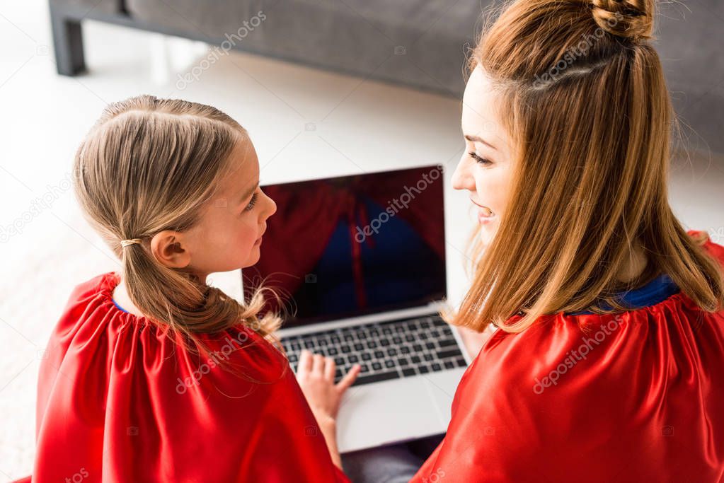 Back view of mother and daughter in red cloaks holding laptop