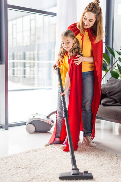 mother and kid in red capes with vacuum cleaner looking down 