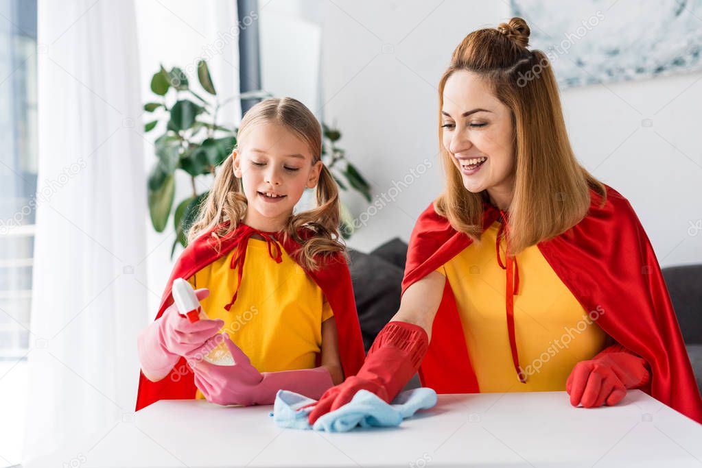Mother and daughter in red capes and rubber gloves dusting at home