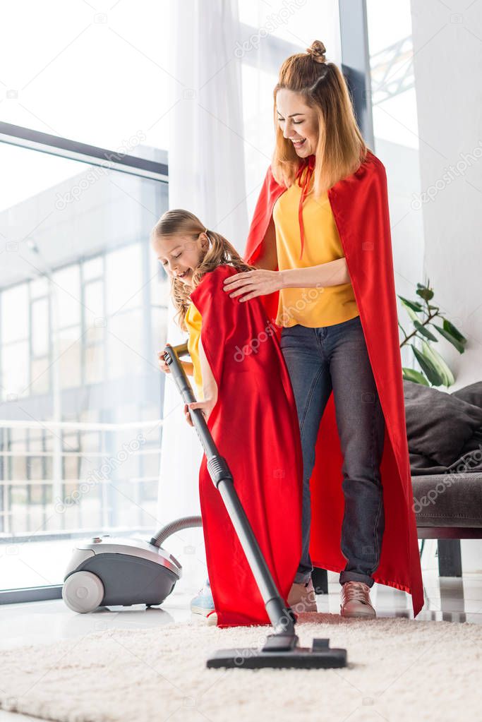 mother and daughter in red capes with vacuum cleaner at home