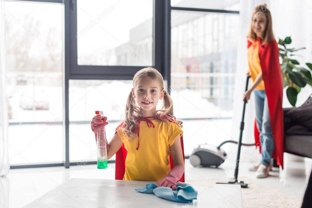 Cute kid dusting and mother with vacuum cleaner at home