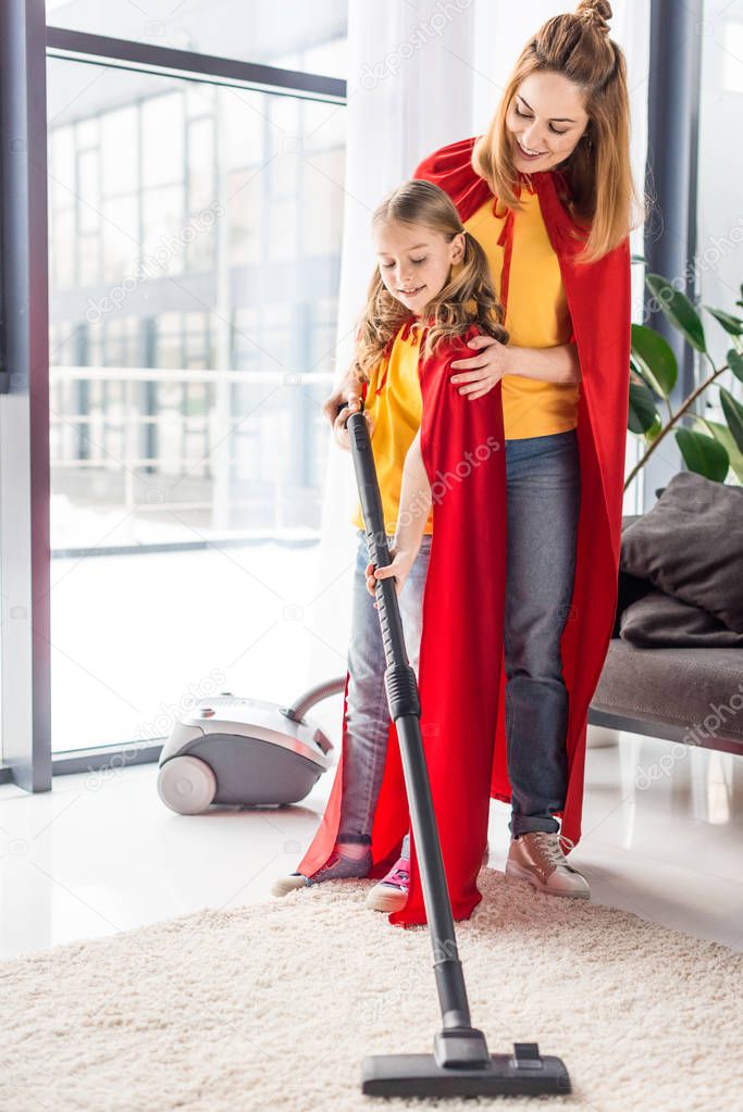 mother and kid in red capes with vacuum cleaner looking down 