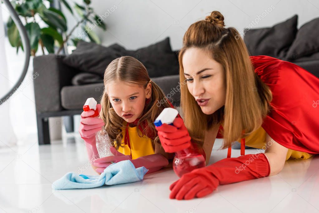 mother and daughter in red capes and rubber gloves washing floor at home