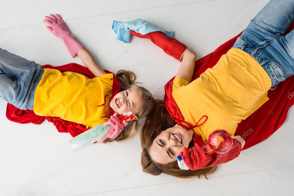 Top view of cheerful mother and kid in red capes and rubber gloves with sprays 