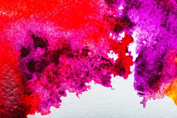 top view of pink, purple and red watercolor spills on white paper