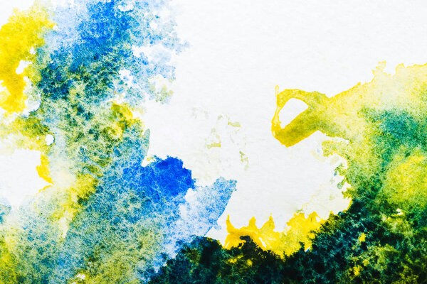 top view of blue and yellow watercolor spills on white paper
