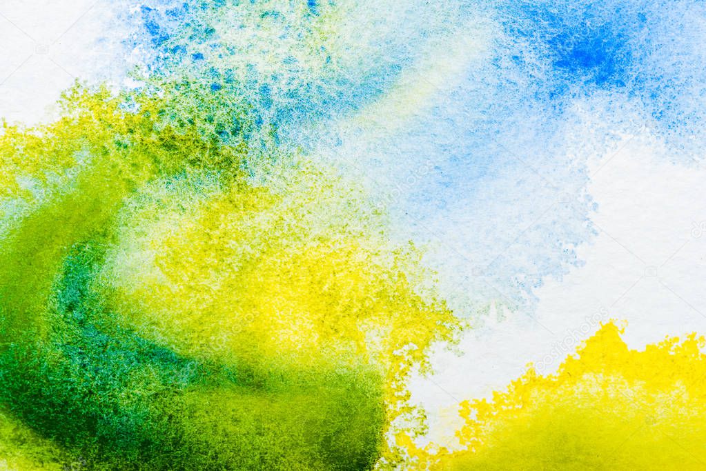 top view of blue, yellow and green watercolor spills on white paper