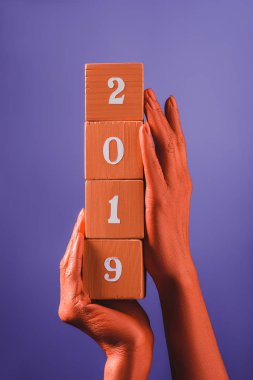partial view of woman holding coral wooden cubes with 2019 numbers on blue background, color of 2019 concept clipart