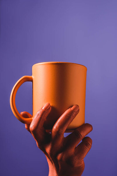 partial view of coral colored female hand with coral coffee cup on violet background,  color of 2019 concept