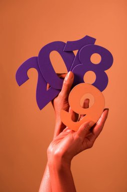 partial view of coral colored female hands with violet paper cut 2018 numbers and coral number 9 on coral background, color of 2019 concept clipart