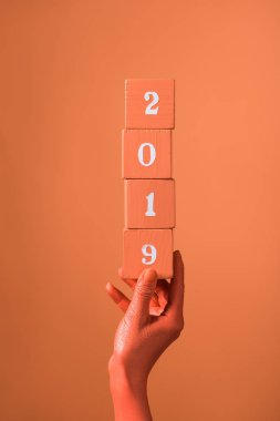 partial view of woman holding coral wooden cubes with 2019 numbers on coral background, color of 2019 concept clipart