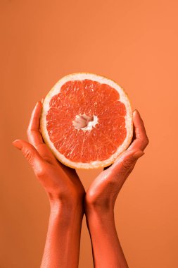 cropped view of coral colored female hands with grapefruit half on coral background, color of  2019 concept clipart