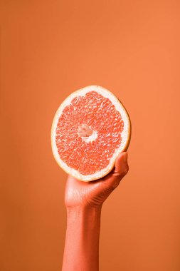 cropped view of coral colored female hand with grapefruit half on coral background, color of 2019 concept clipart