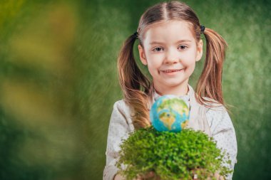 selective focus of smiling child with flower pot and globe model on blurred background, earth day concept clipart