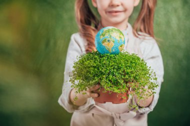 selective focus of kid holding flower pot with plant and globe model on blurred background, earth day concept clipart