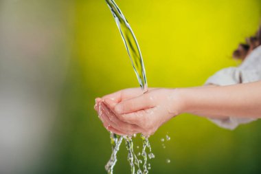 cropped view of child holding hands under flowing water on blurred background, earth day concept clipart