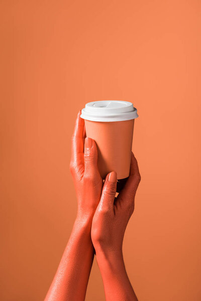 cropped view of woman holding coral paper cup on coral background, color of 2019 concept