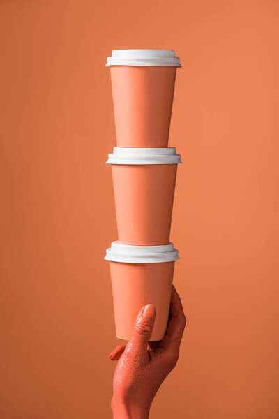 cropped view of female hand with stack of coral paper cups on coral background, color of 2019 concept