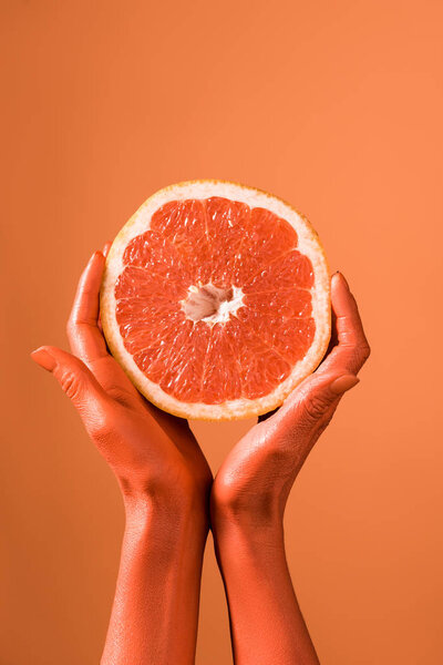 cropped view of coral colored female hands with grapefruit half on coral background, color of  2019 concept