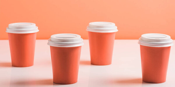 coral paper cups arranged on white surface on coral background, color of 2019 concept