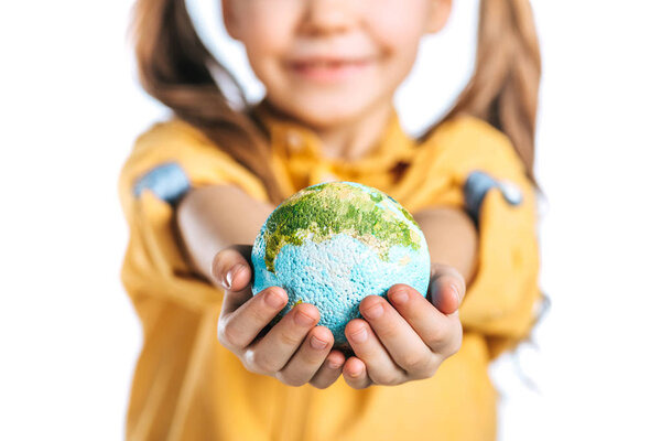 selective focus of cute child holding globe model in stretched hands isolated on white, earth day concept