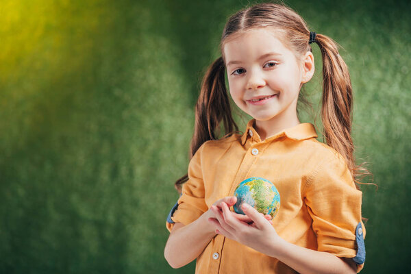 cute smiling child holding globe model near heart on blurred background, earth day concept