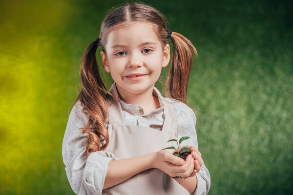 cute child holding young green plant on blurred background, earth day concept