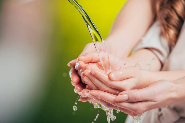 selective focus of woman and child holding hands under flowing water on blurred background, earth day concept