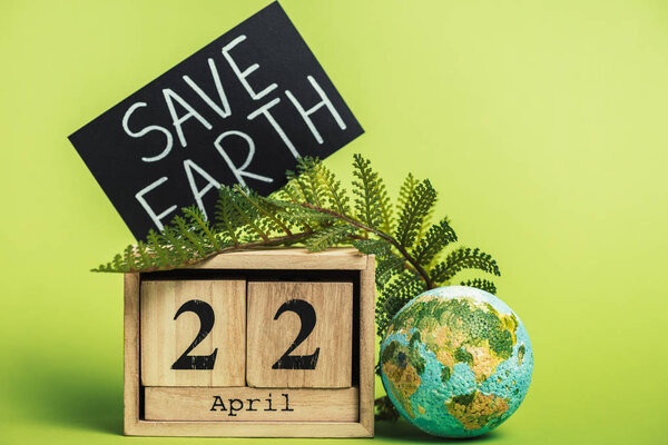 wooden calendar with date "22 april" and green fern leaf on light green background