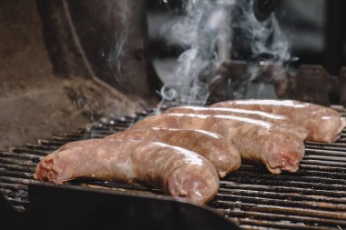 selective focus of raw sausages cooking on bbq grill with smoke clipart