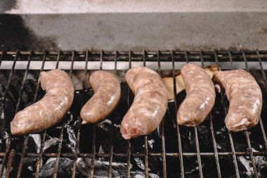 raw fresh sausages cooking on barbecue grill grate with burning coals clipart
