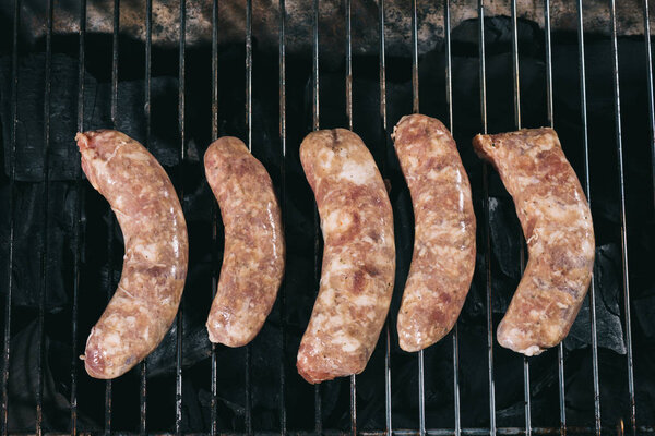 top view of raw pork sausages cooking on barbecue grill grates 