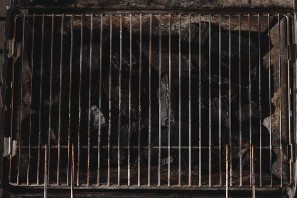 top view of dark black natural coals under iron bbq grid