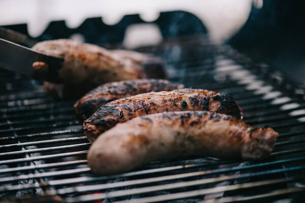 selective focus of grilled meat sausages and tweezers on barbecue grid