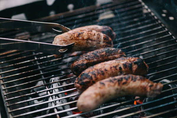 grilled delicious meat sausages and tweezers on barbecue grid