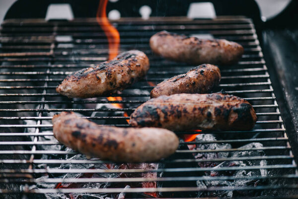 selective focus of grilled scattered delicious sausages in flame on bbq grid